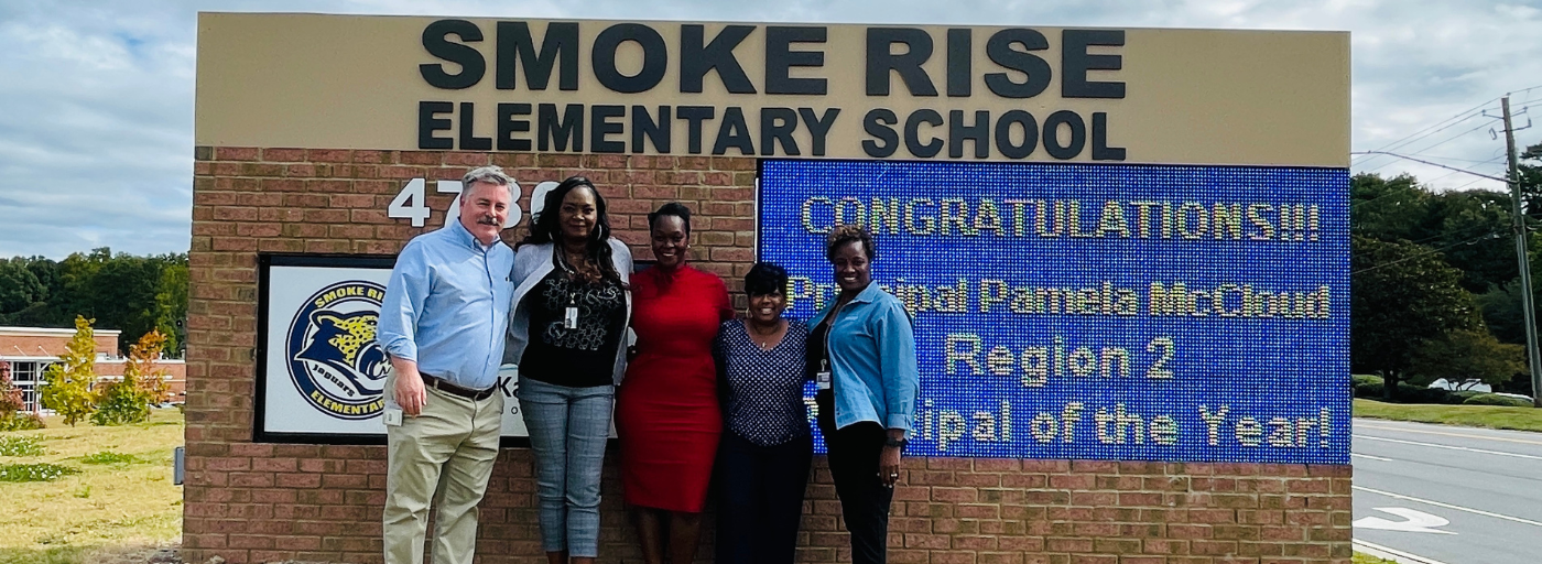 4 district staff members with the principal Pamela McCloud in front of the outside digital marquee sign.