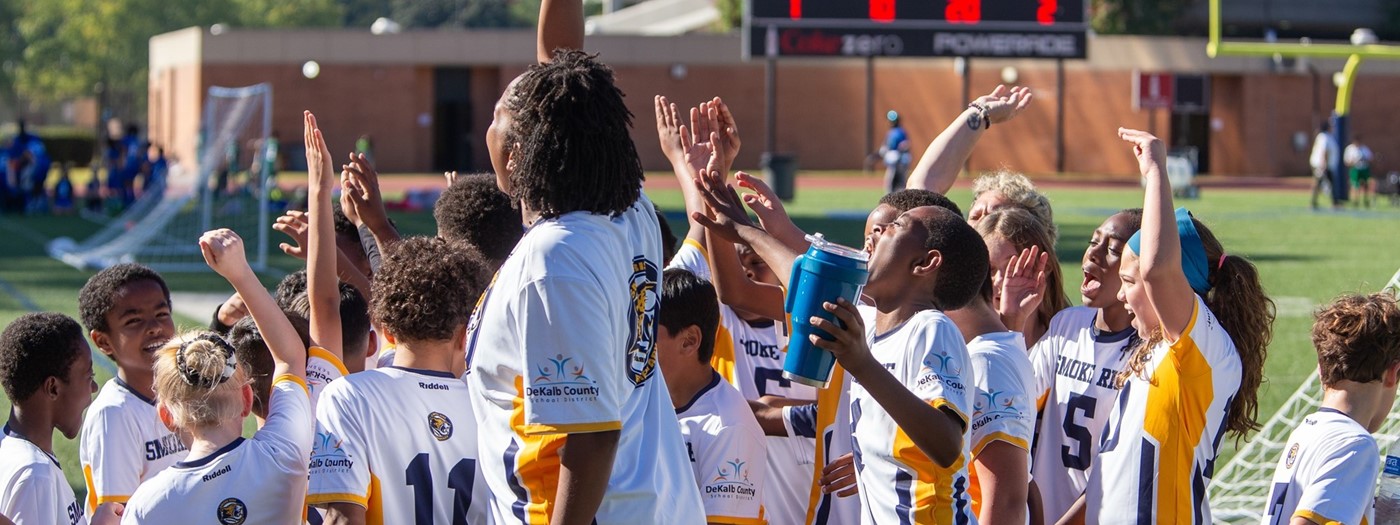 Soccer team in a huddle smiling and raising their hands.