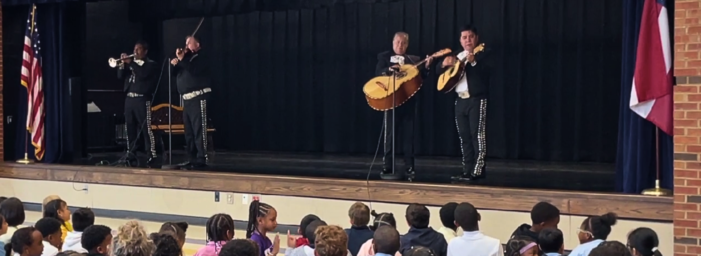 A mariachi band performs on stage in front of a crowd of students.