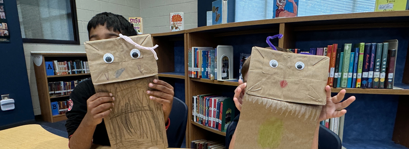 Two students holding up paper bag puppets