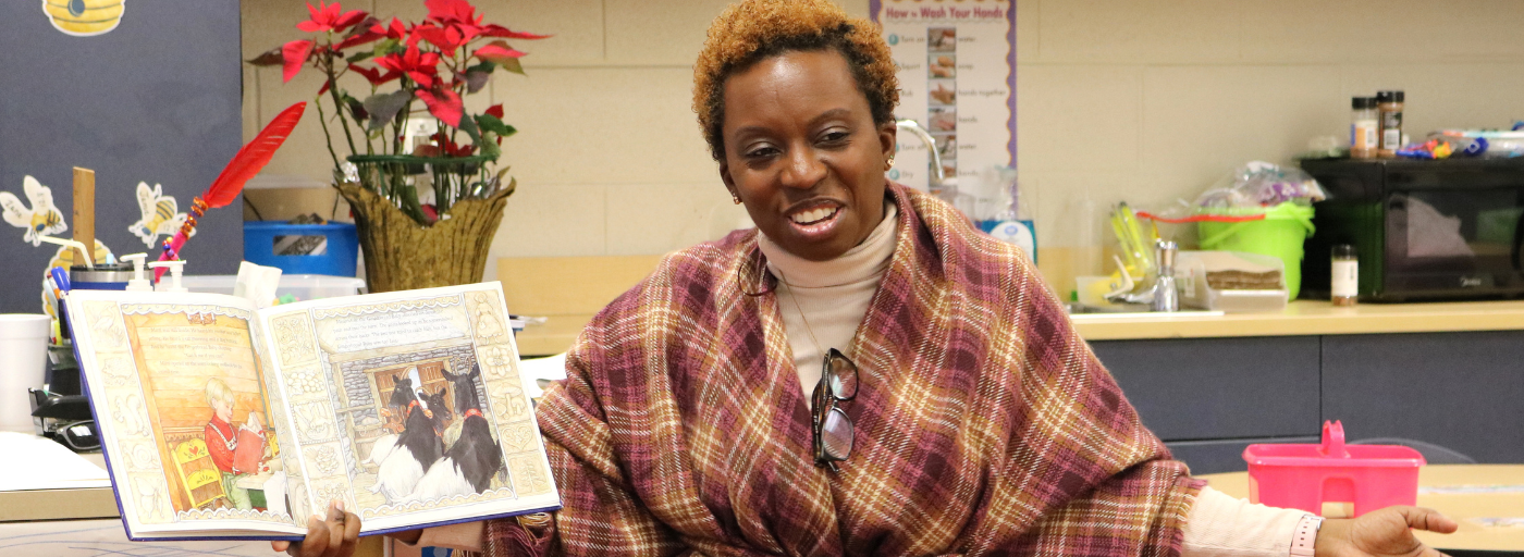 Teacher holding a storybook with her arms stretched out. 